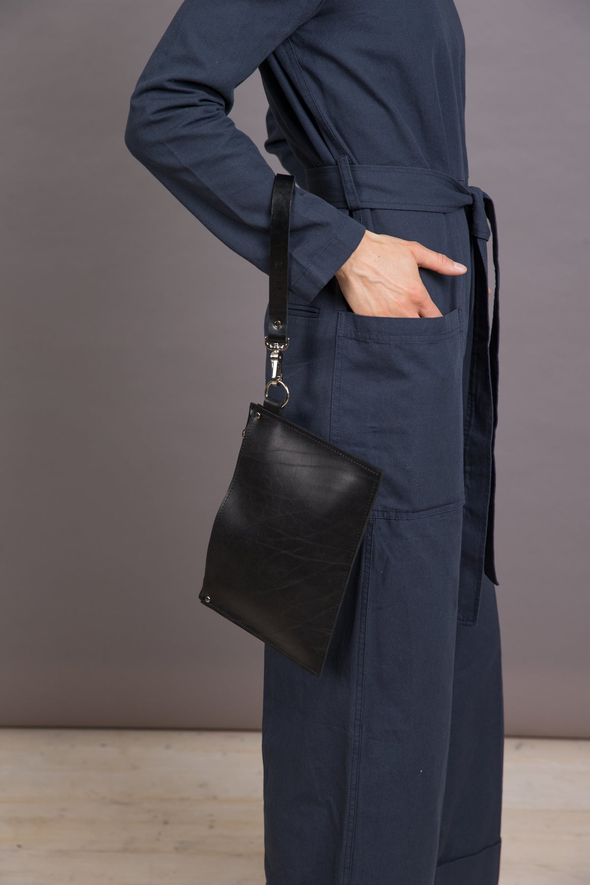 Schwarze PYKOK Nina Leder-Clutch am Handgelenk getragen